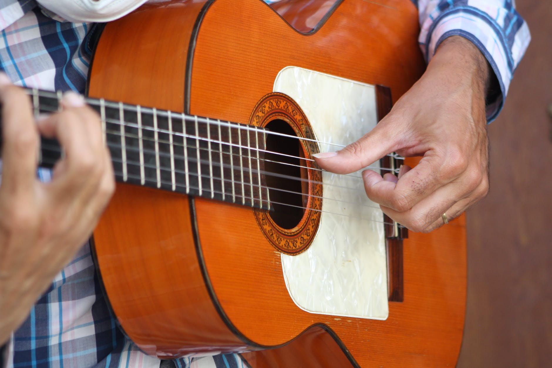 osoba hrající hnědou akustickou kytaru